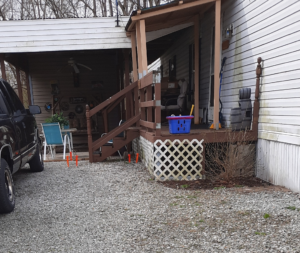 image of a brown wooden porch outside a grey home with three steps and the ground is grey gravel